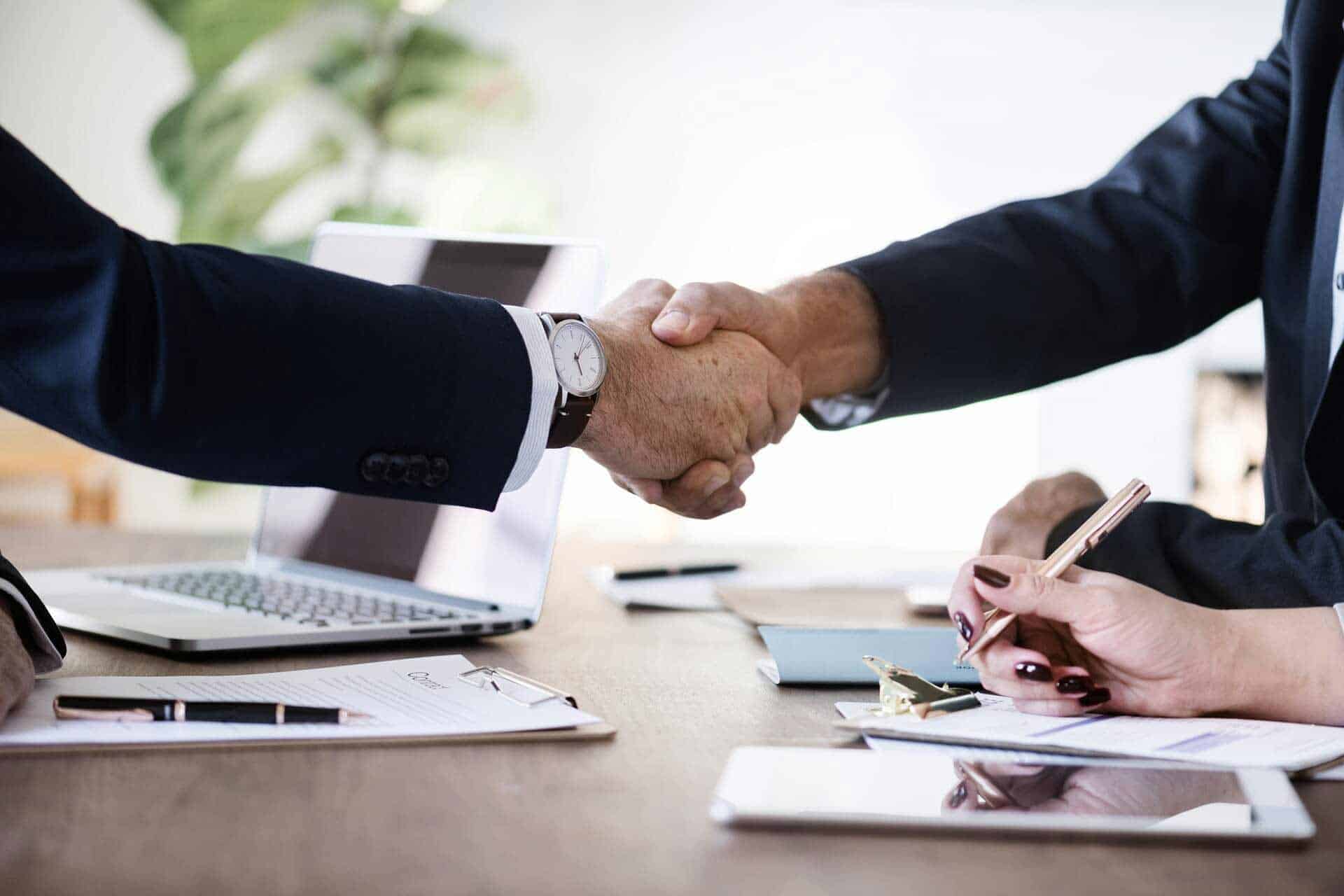 Two men shaking hands over a desk during a business deal